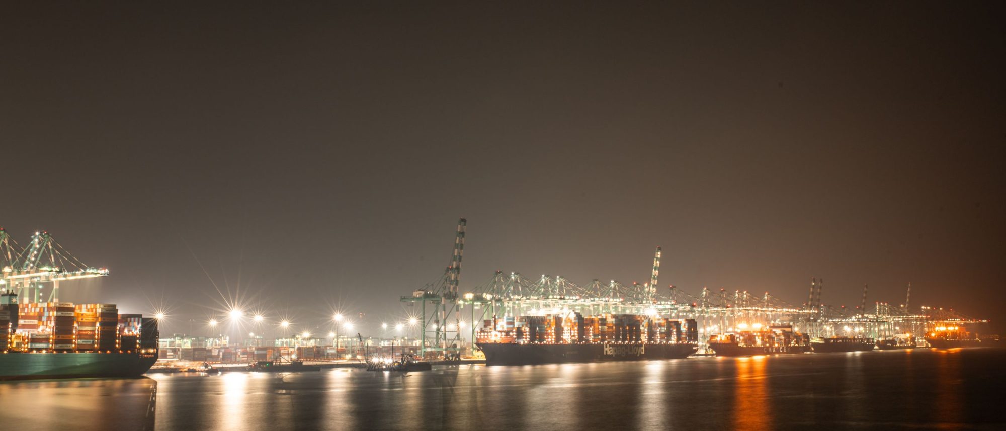 A container port lit at night with cargo ships moored along the quay.