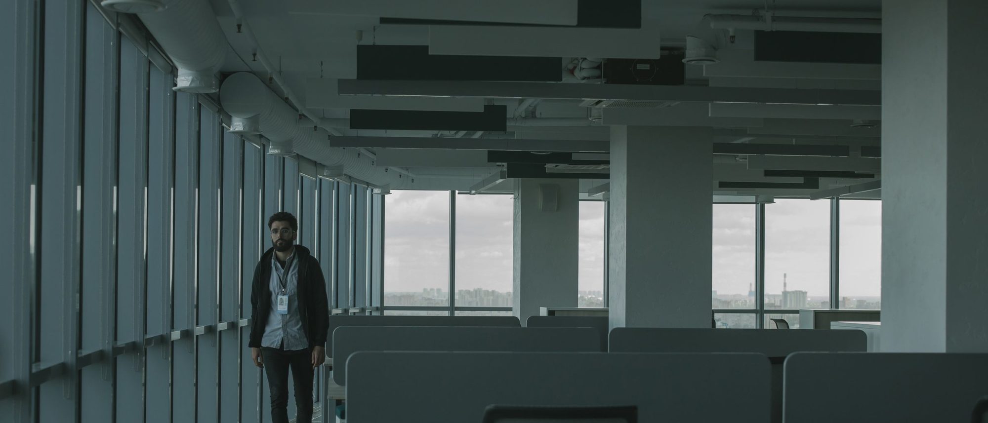 A single figure walking through a dim and empty open-plan office.