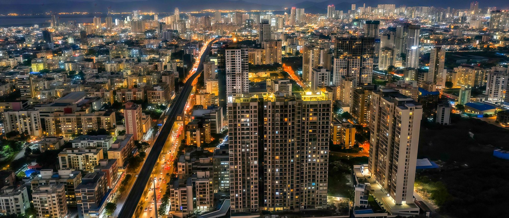 Mumbai’s residential towers and a lit arterial road seen from high above at night.