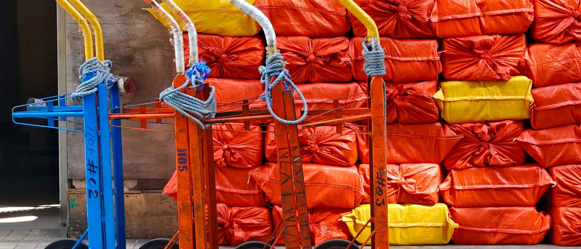 Hand trucks stand in a row against stacked sacks in a warehouse.
