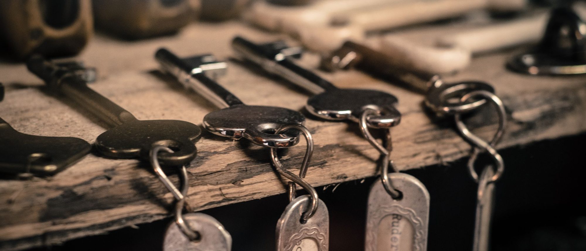 Old metal keys on rings hanging from hooks on a weathered wooden board.