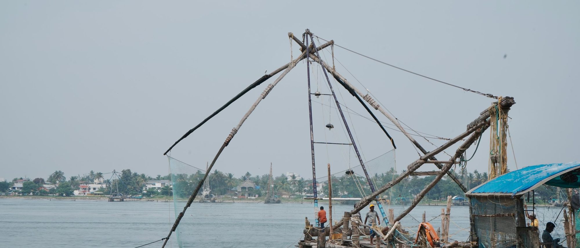 Chinese fishing nets stand over the water at Kochi while fishermen work on the shore.