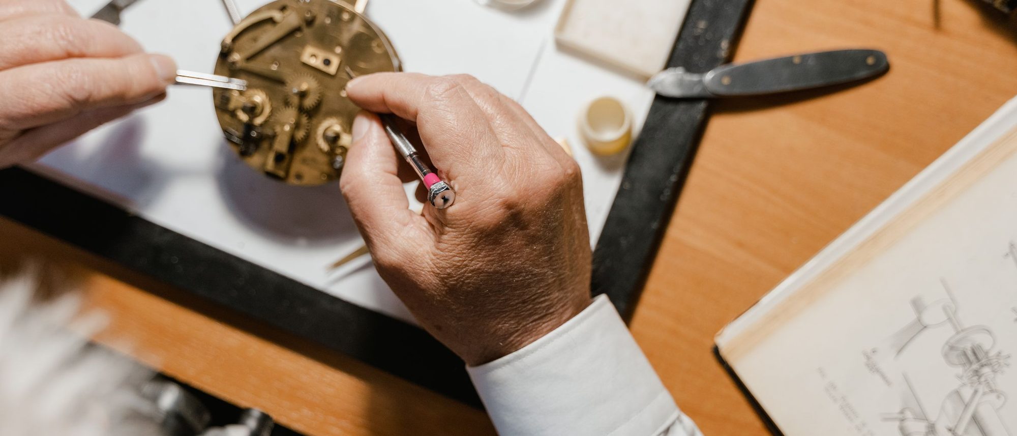 A watchmaker's tools and the parts of an opened watch lie on a wooden bench.