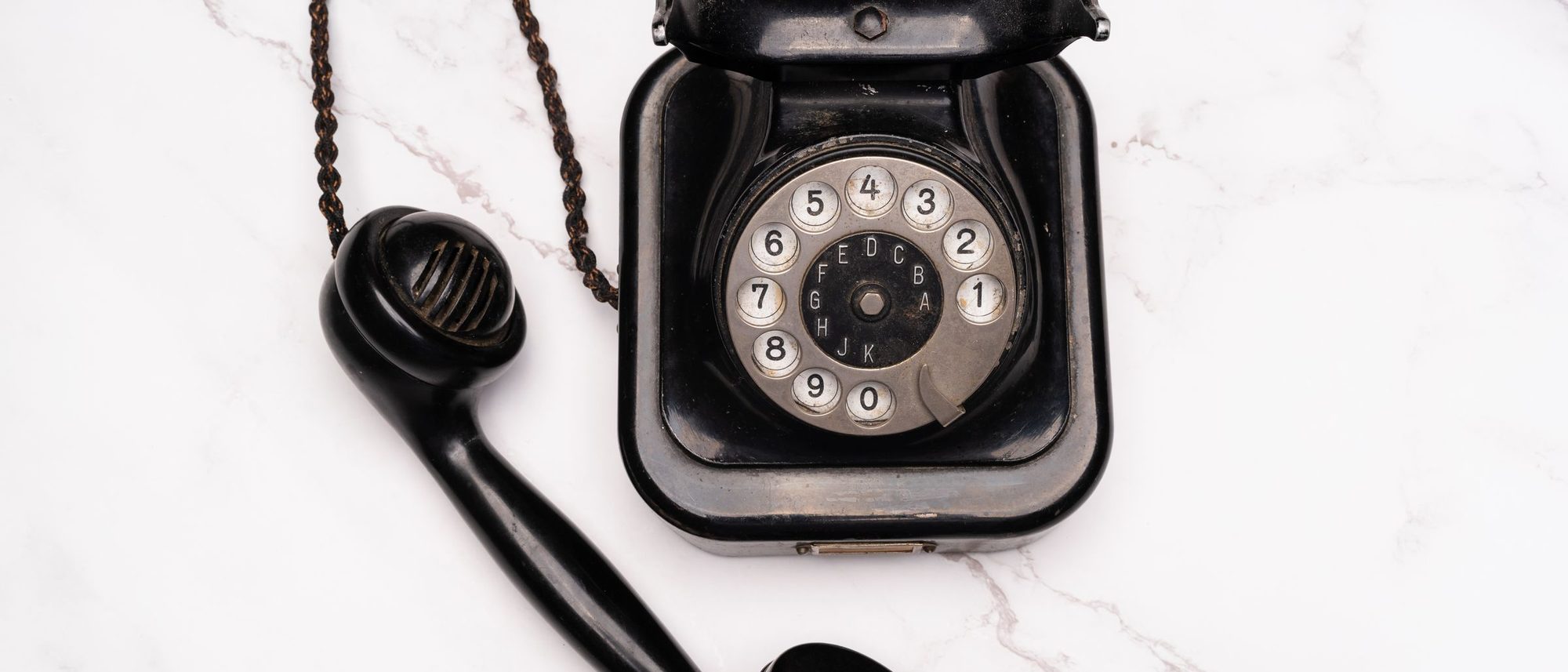 An old rotary dial telephone with its receiver rests on white marble.