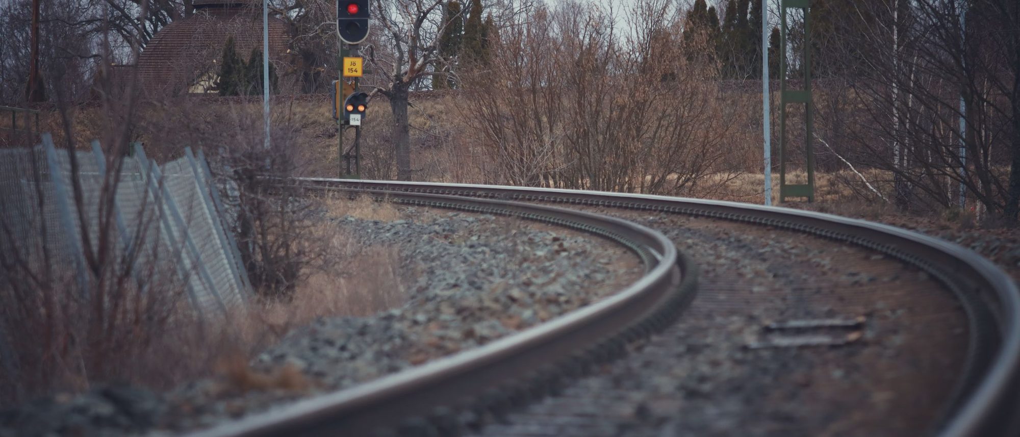 A railway line curving through a winter landscape of bare trees towards a distant signal.