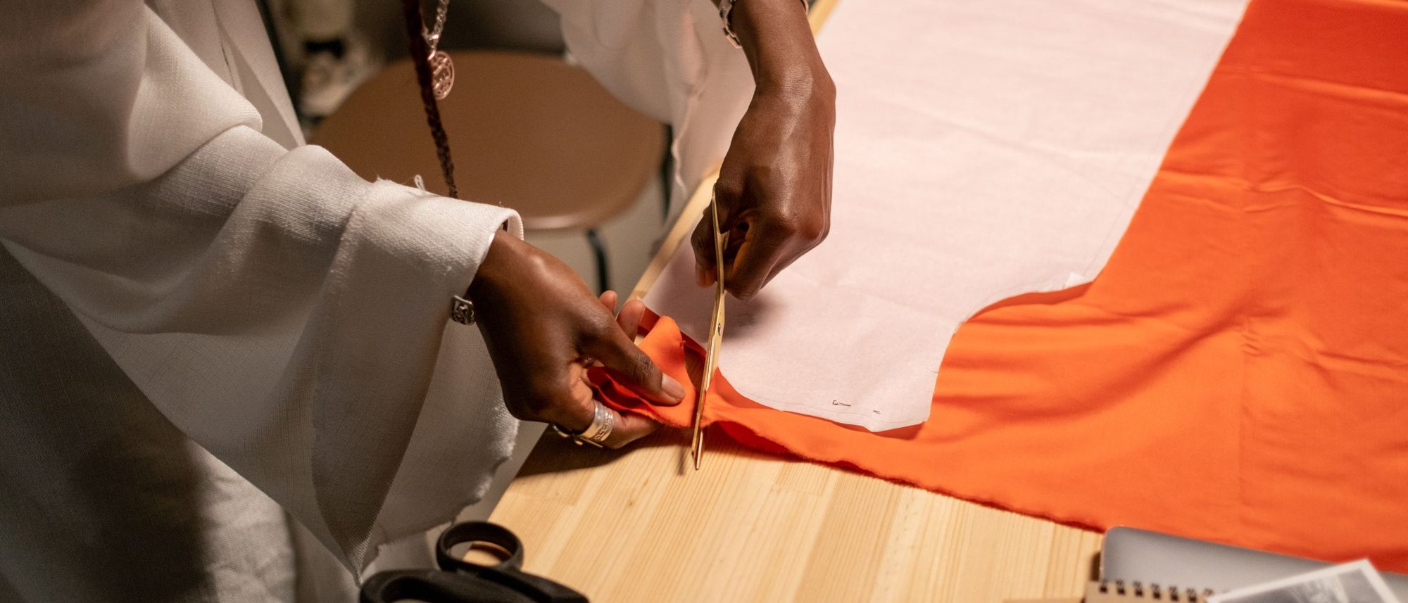 A designer cuts fabric along the lines of a paper pattern laid on a studio table.