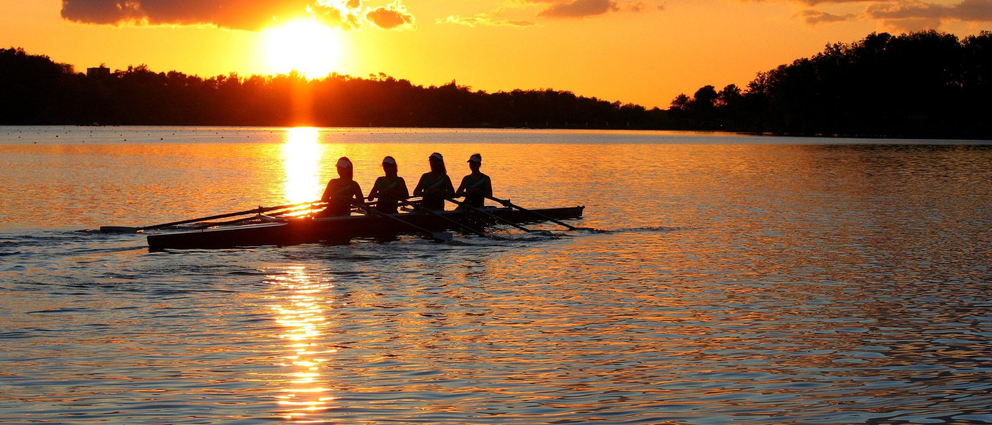 Four rowers in silhouette on a lake at sunset.