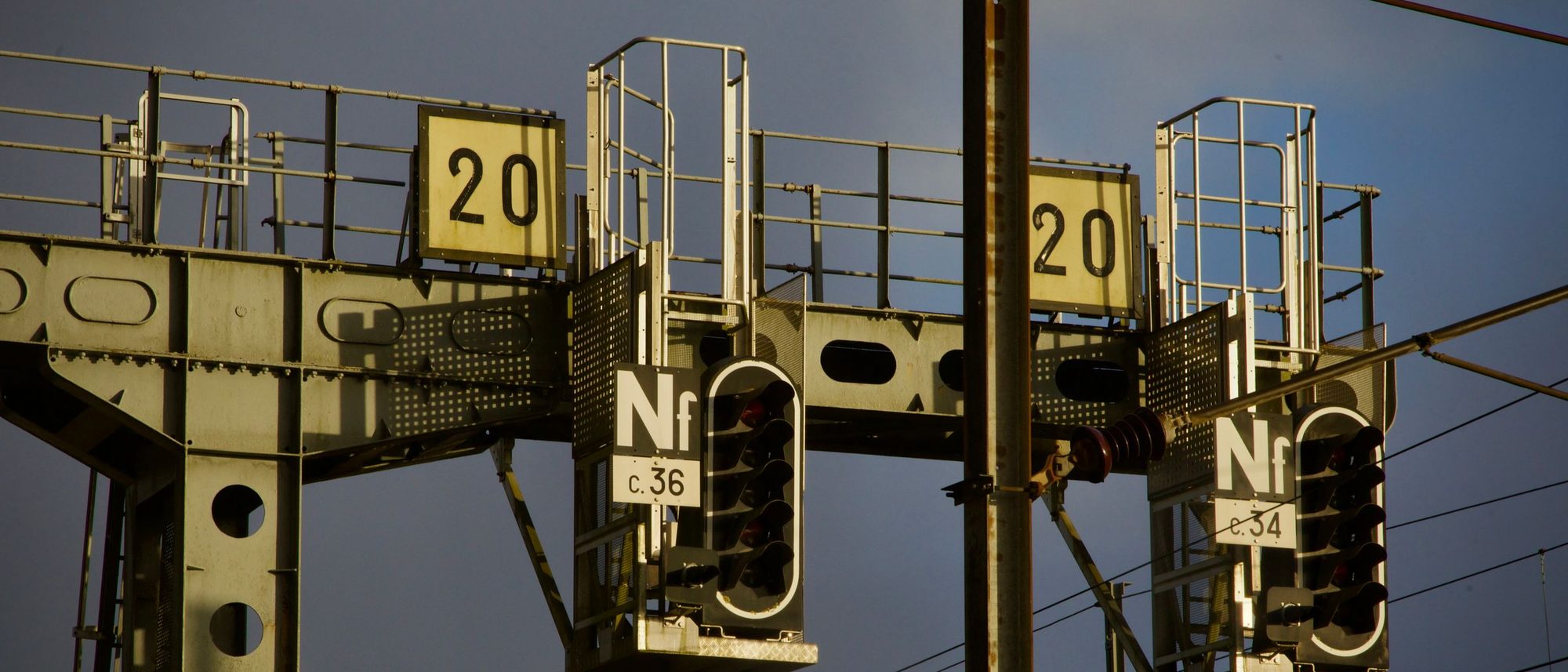 A railway signal gantry with lit indicators against a dusk sky.