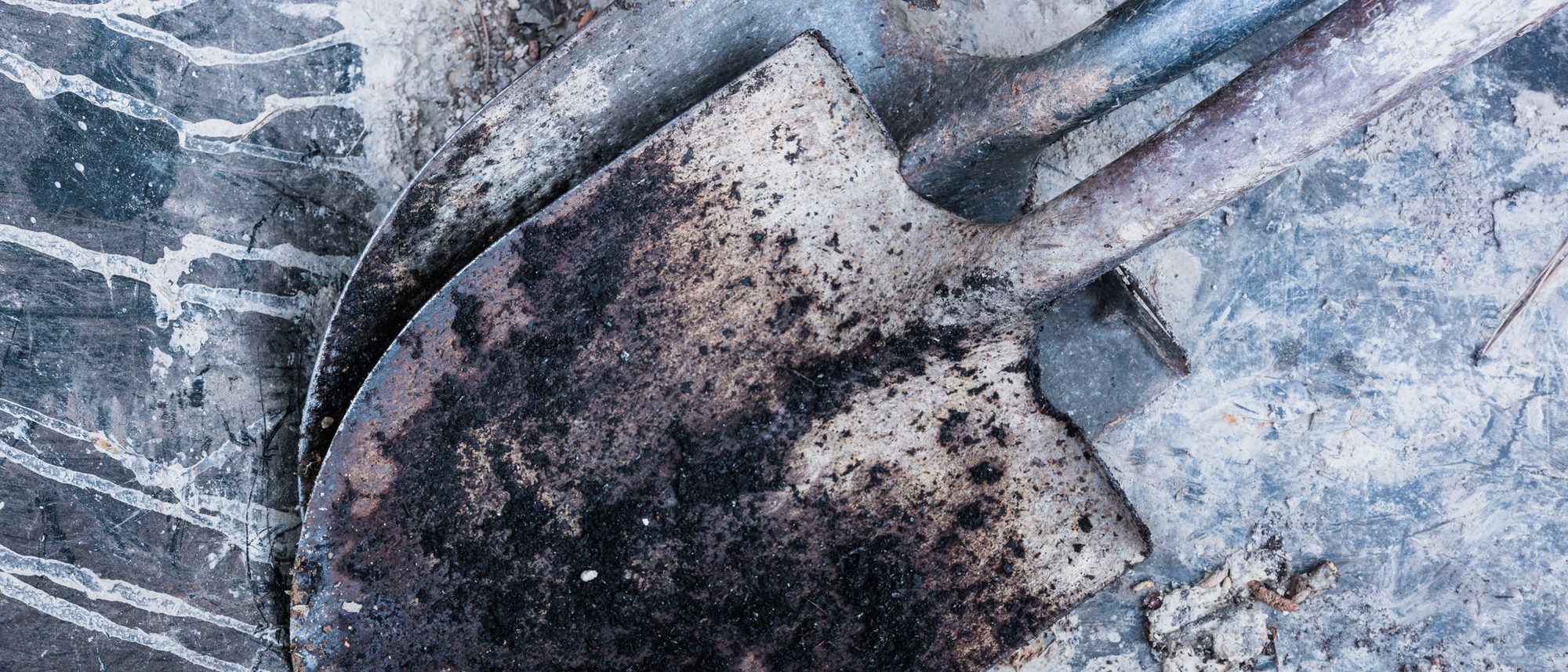 Worn and rusted shovels lying on a concrete floor.