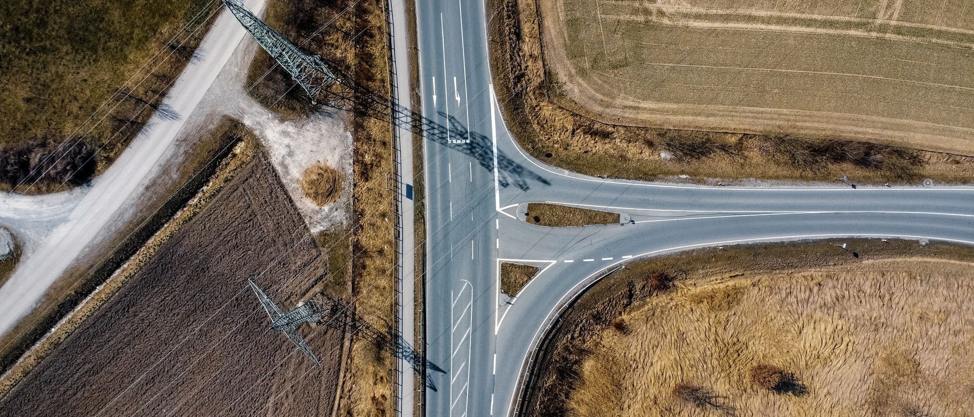 An aerial view of two farm roads meeting among green fields with a line of power poles.