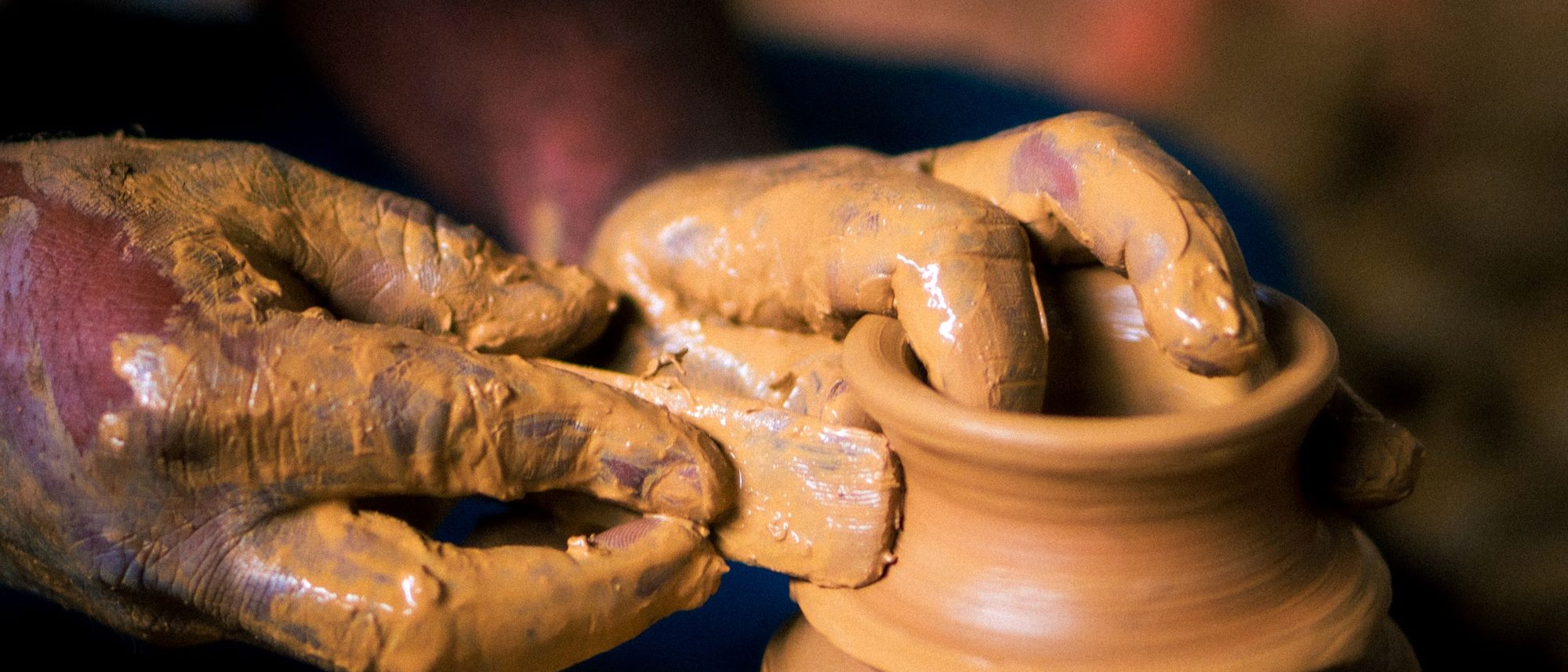 Clay-covered hands shape a pot on a spinning potter’s wheel.