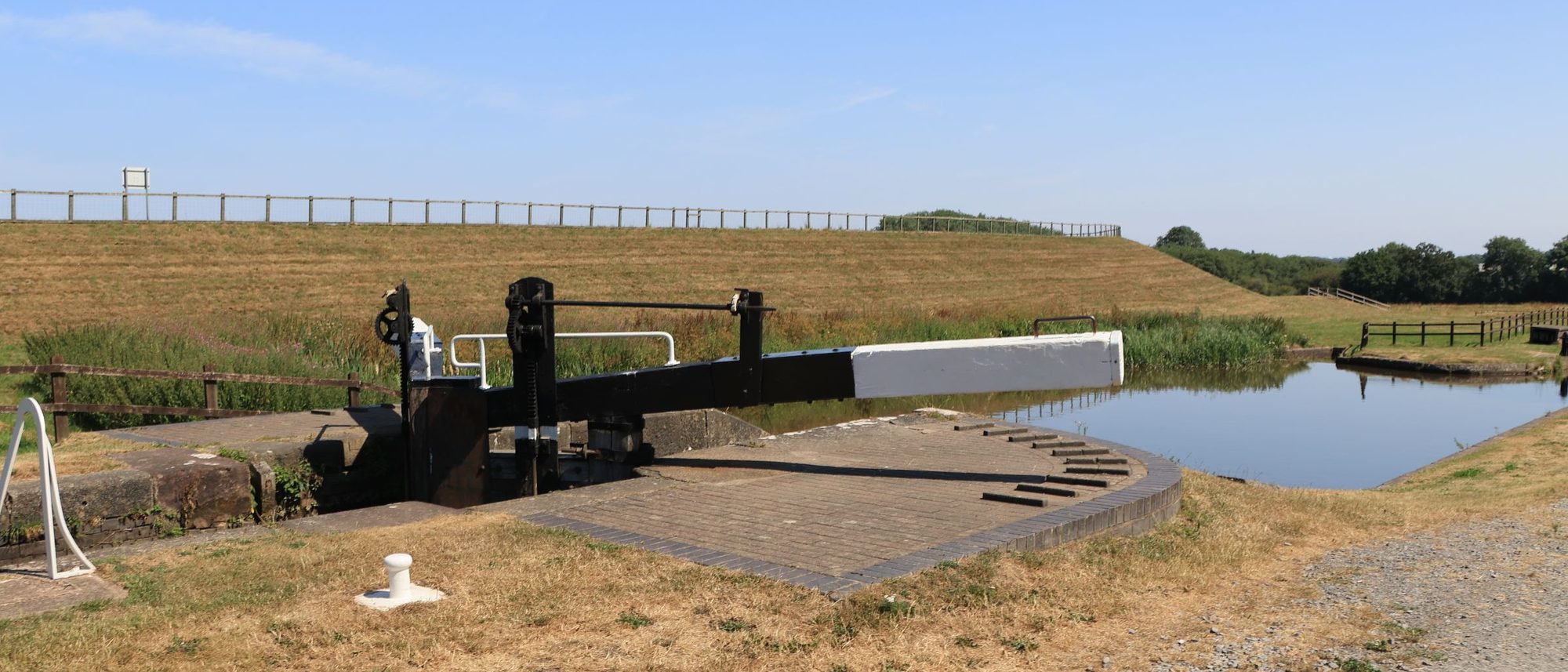 A canal lock gate with its black and white balance beam under a clear summer sky.