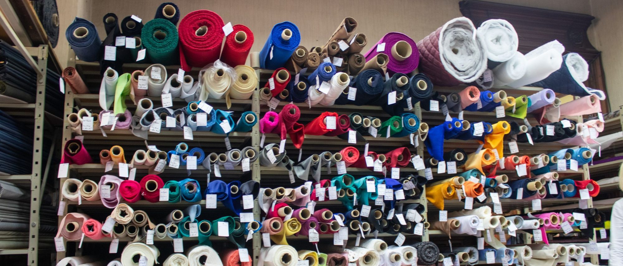 Rolls of fabric in many colours stacked on the shelves of a shop.