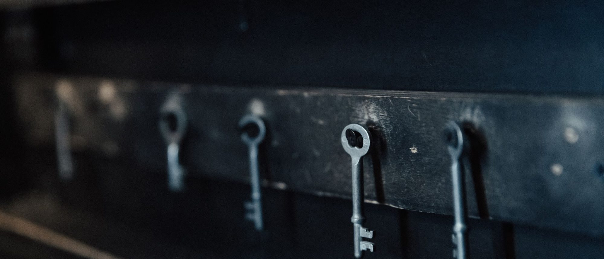 Antique metal keys hang in a row against a dark wall.