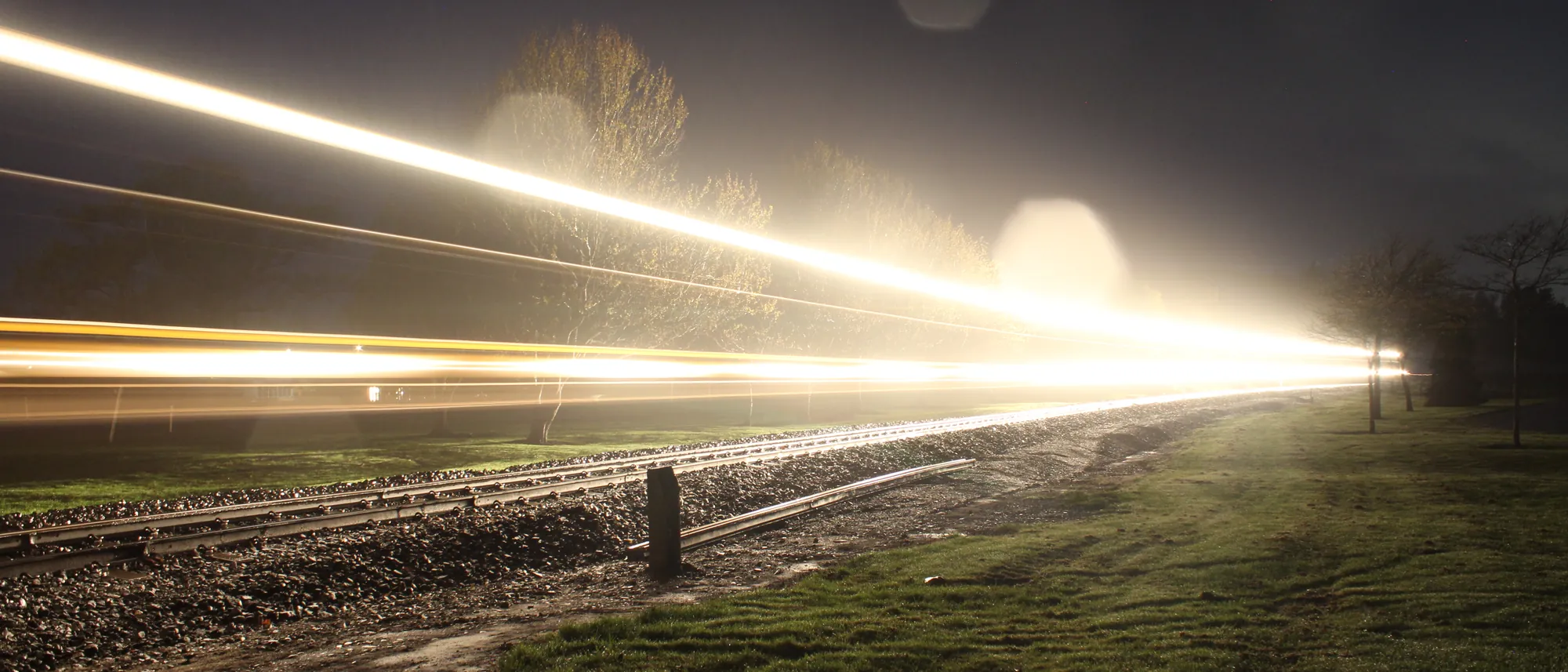 A train at night drawn as one long beam of light across a dark field, a long exposure
