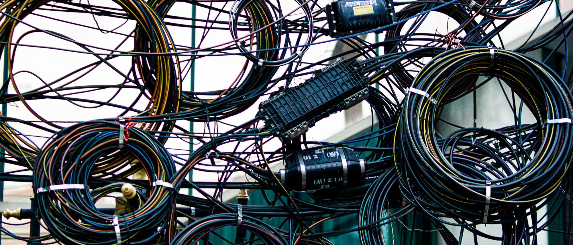 A dense tangle of power and communication cables strung between poles outdoors.