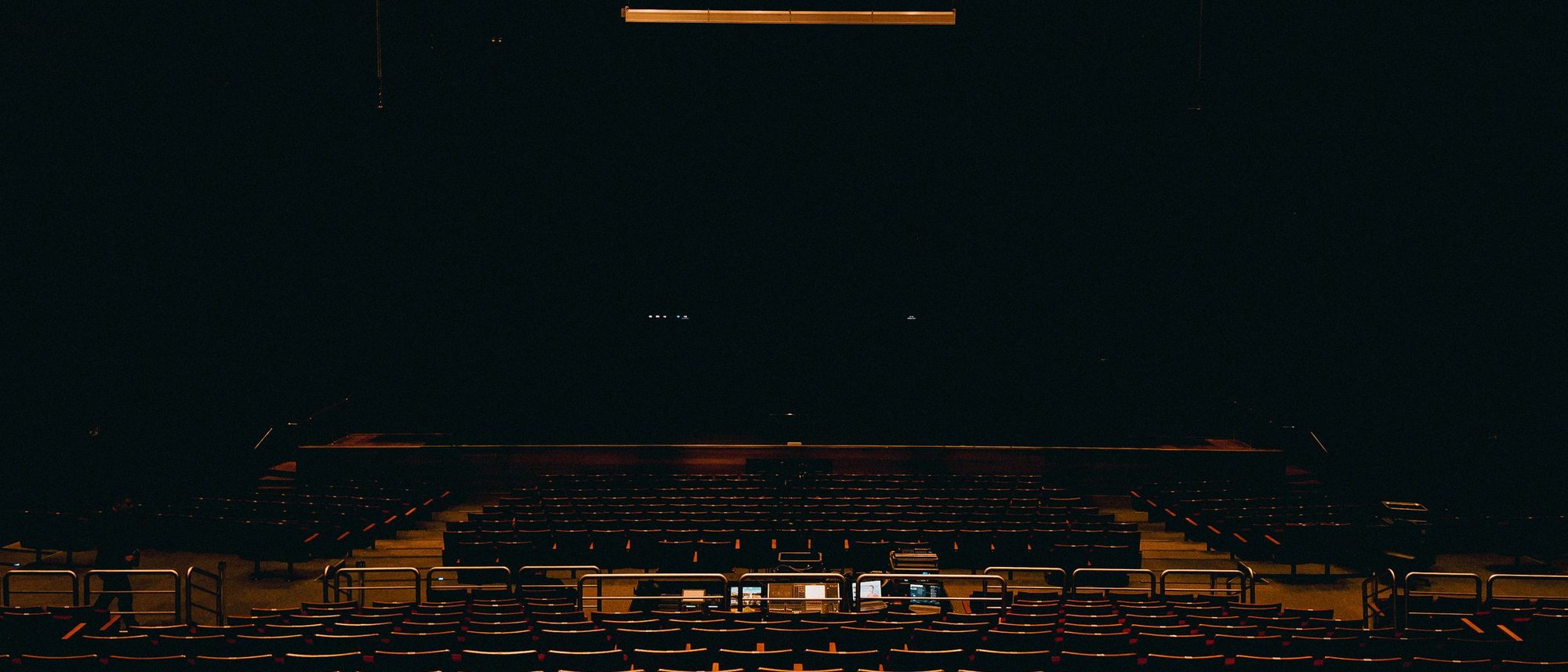 A dark empty auditorium with rows of seats facing a stage.