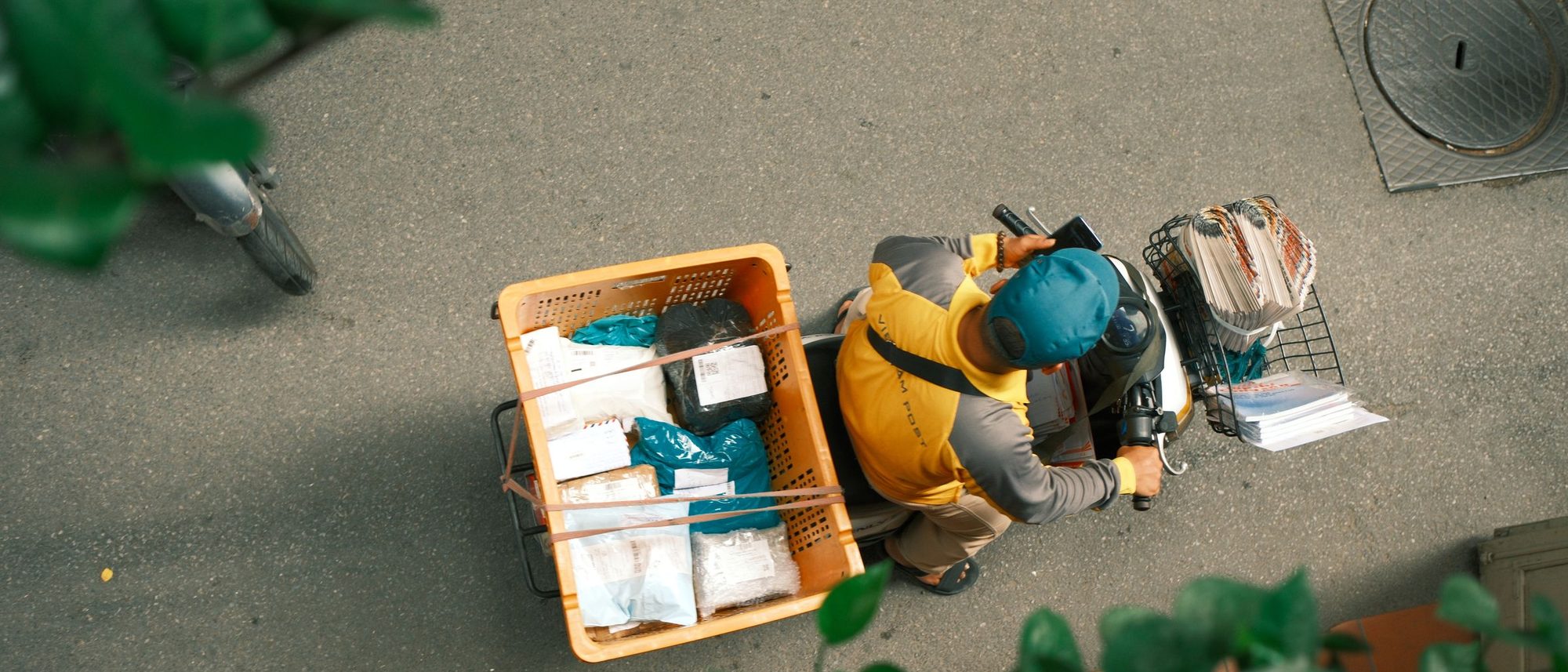 Seen from above a courier on a scooter carries parcels along a sunlit street.
