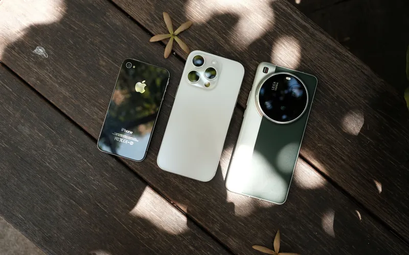Three smartphones lying side by side on a wooden table in dappled sunlight