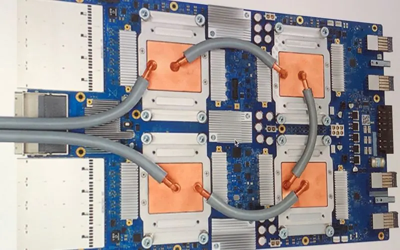 A Google Tensor Processing Unit 3.0 board: four copper-capped chips joined by grey cooling tubes on a blue circuit board