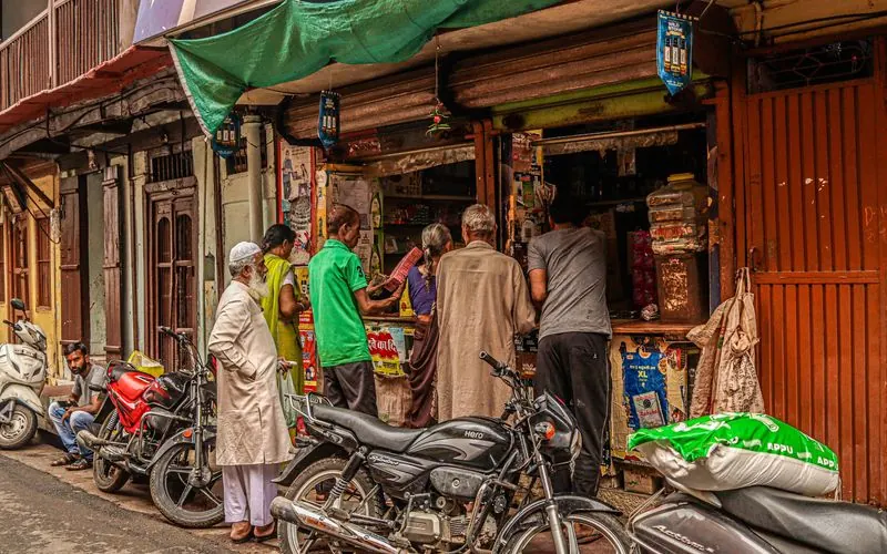 A busy street shop in India with customers at the counter and motorcycles parked outside.
