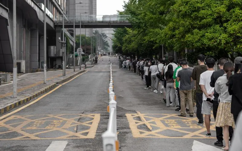 A long queue of people seen from behind, stretching down a city street