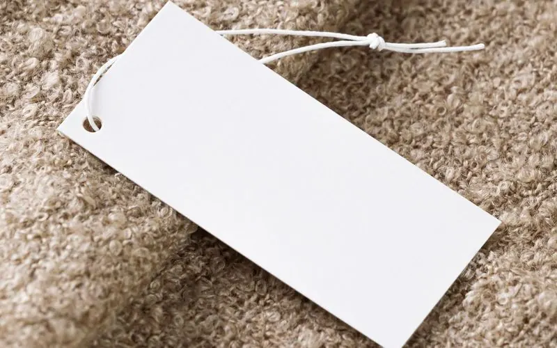 A blank white price tag on string lying on beige fabric