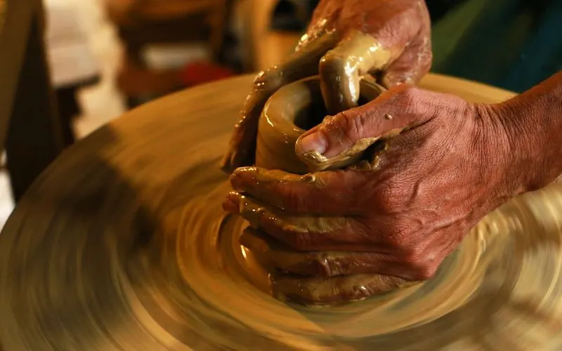 Hands shape wet clay on a spinning pottery wheel.