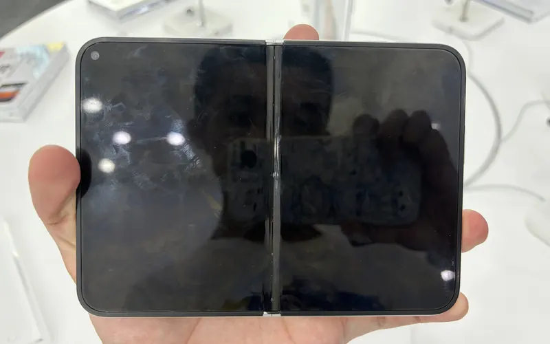An unfolded iPhone Duo held in one hand above a white display table in an Apple store