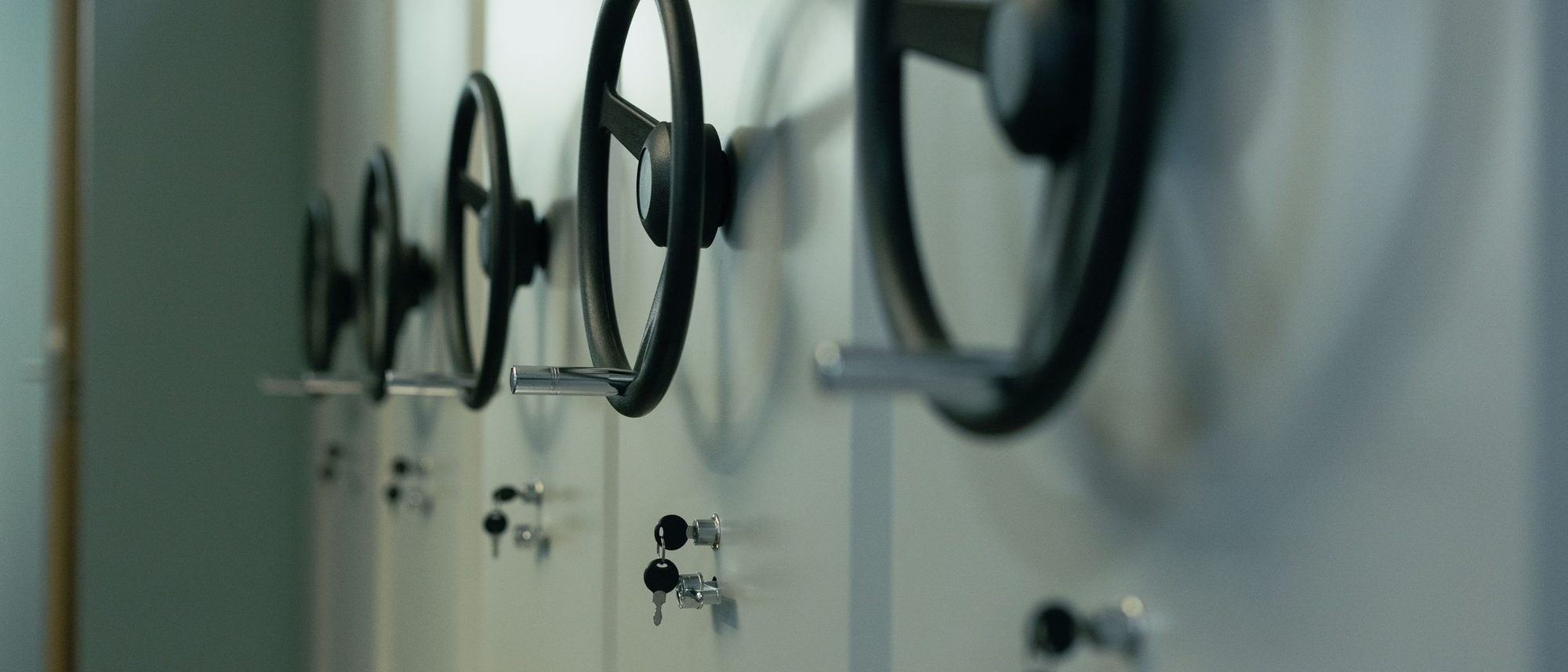 A row of steel safe doors with wheel handles and keys in their locks.