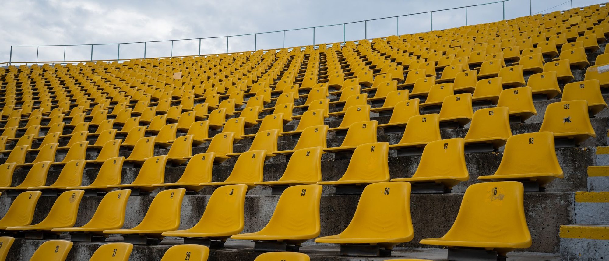 Rows of empty yellow stadium seats under a cloudy sky.