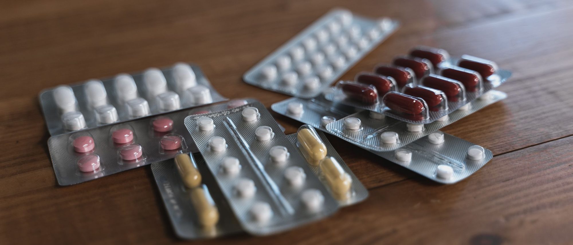 Blister packs of assorted tablets lie on a wooden table.