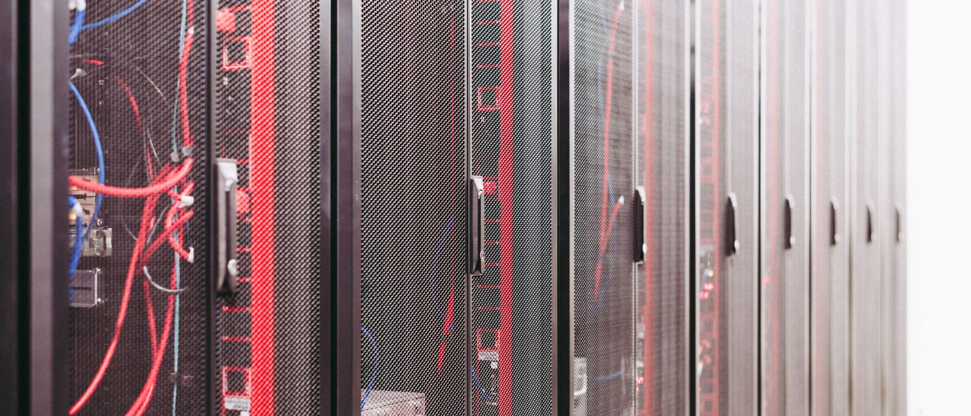 Rows of black server racks and cabling stand in a lit data centre aisle.