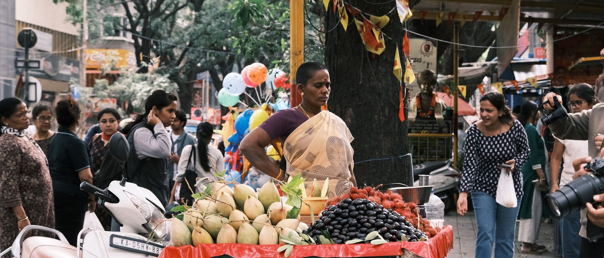 A busy street market in Bengaluru with shoppers around a fresh produce stall.