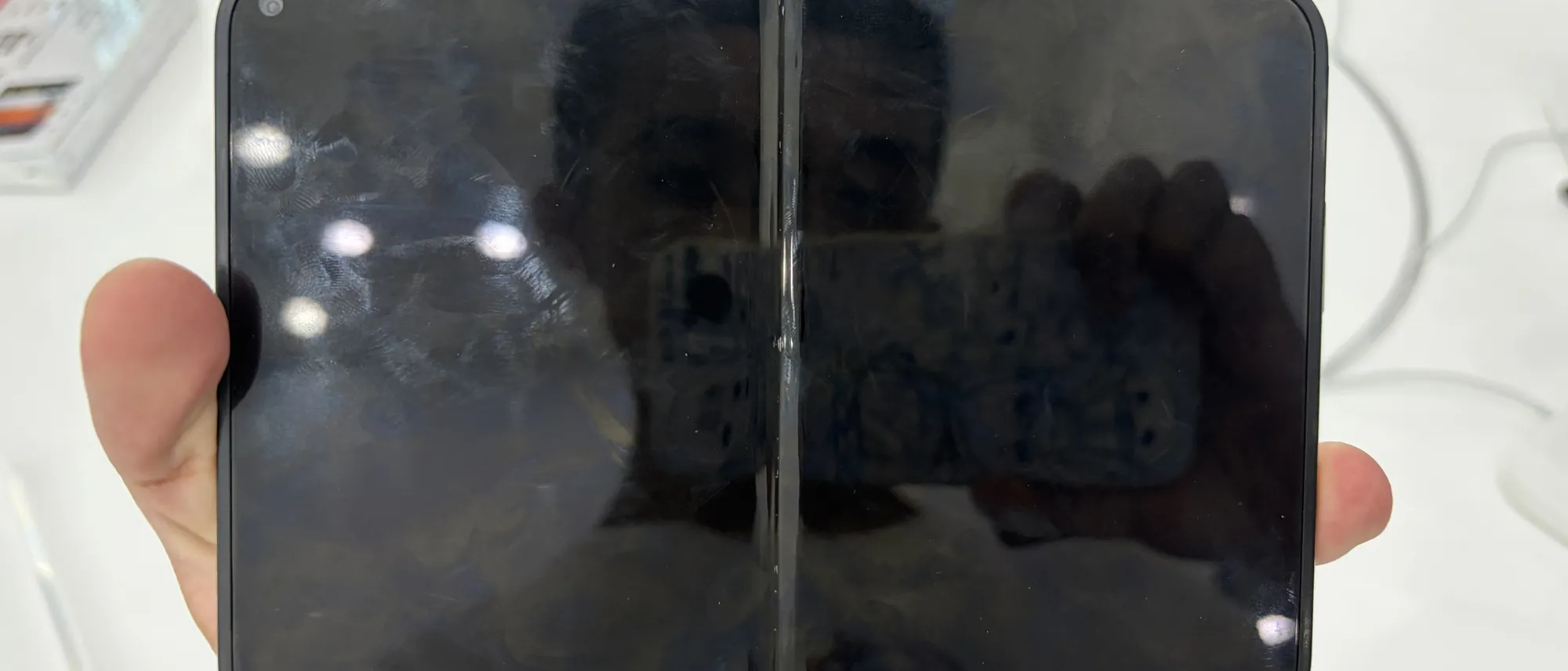 An unfolded iPhone Duo held in one hand above a white display table in an Apple store